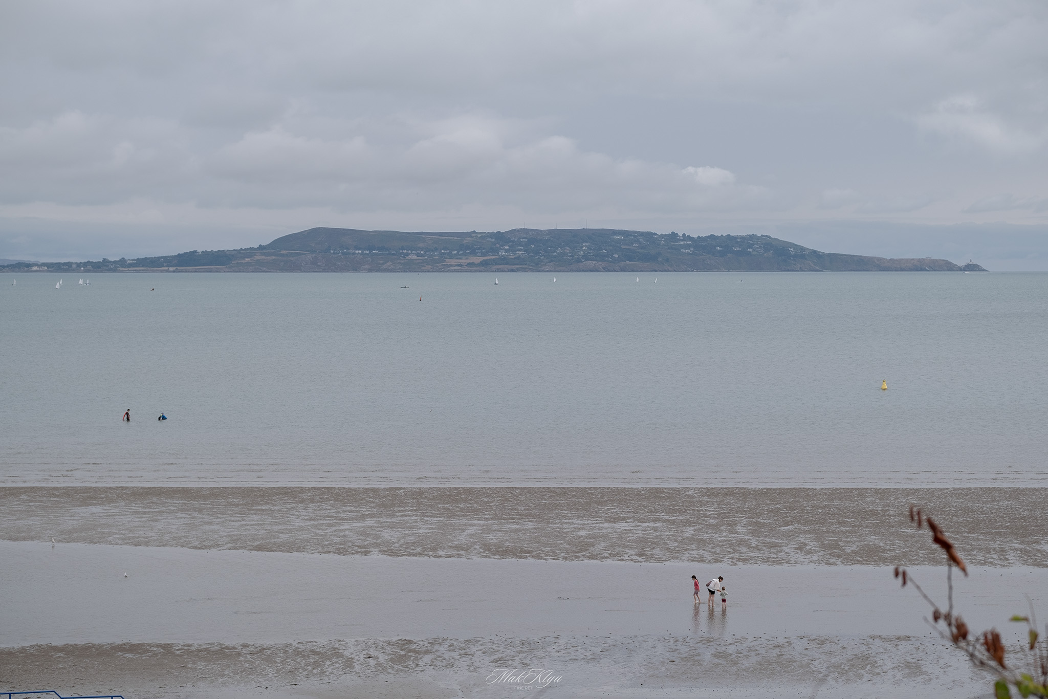 Quiet Irish bay with distant hills and small sailboats beneath a cloudy sky
