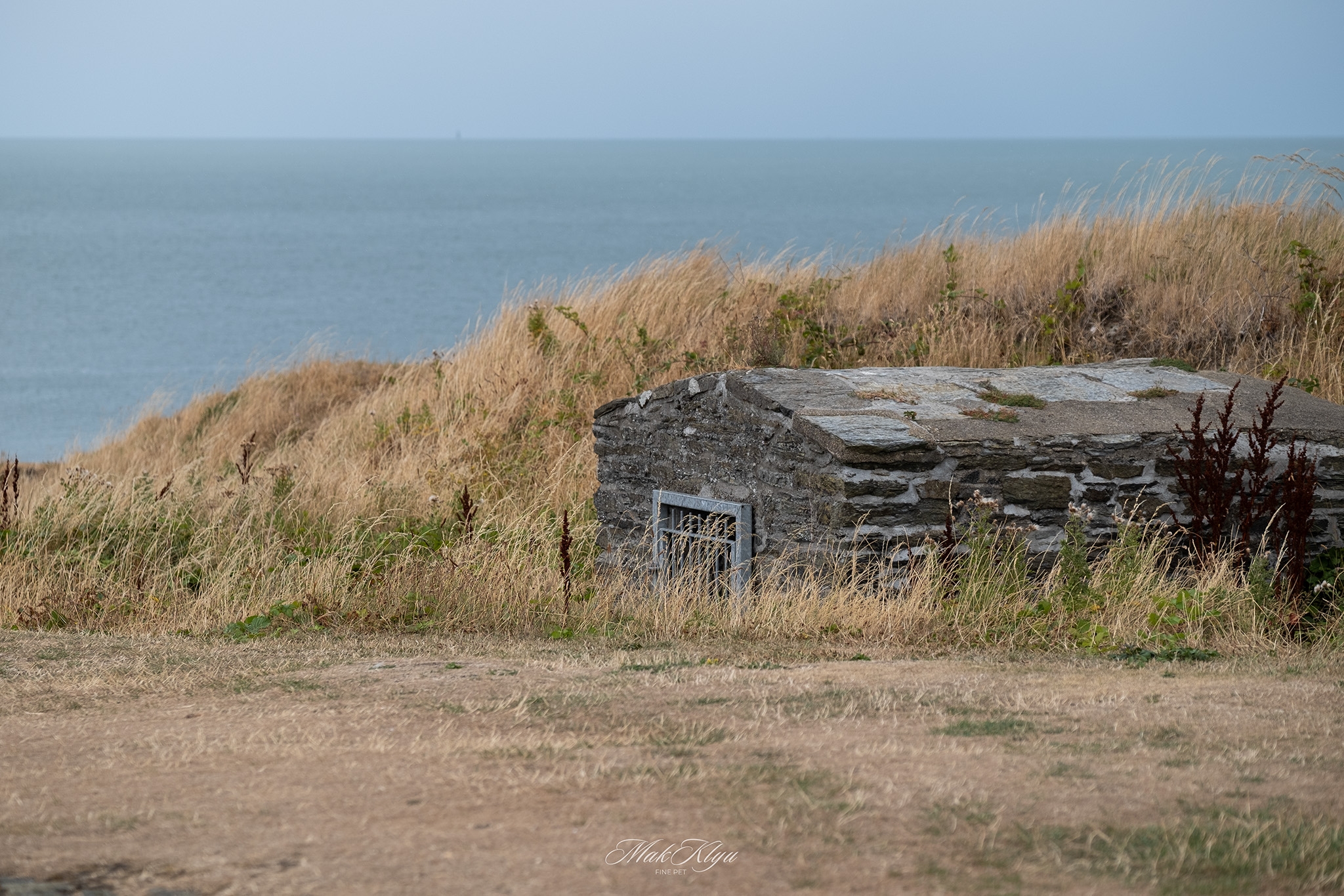 Weathered stone structure surrounded by dry coastal grass overlooking the sea