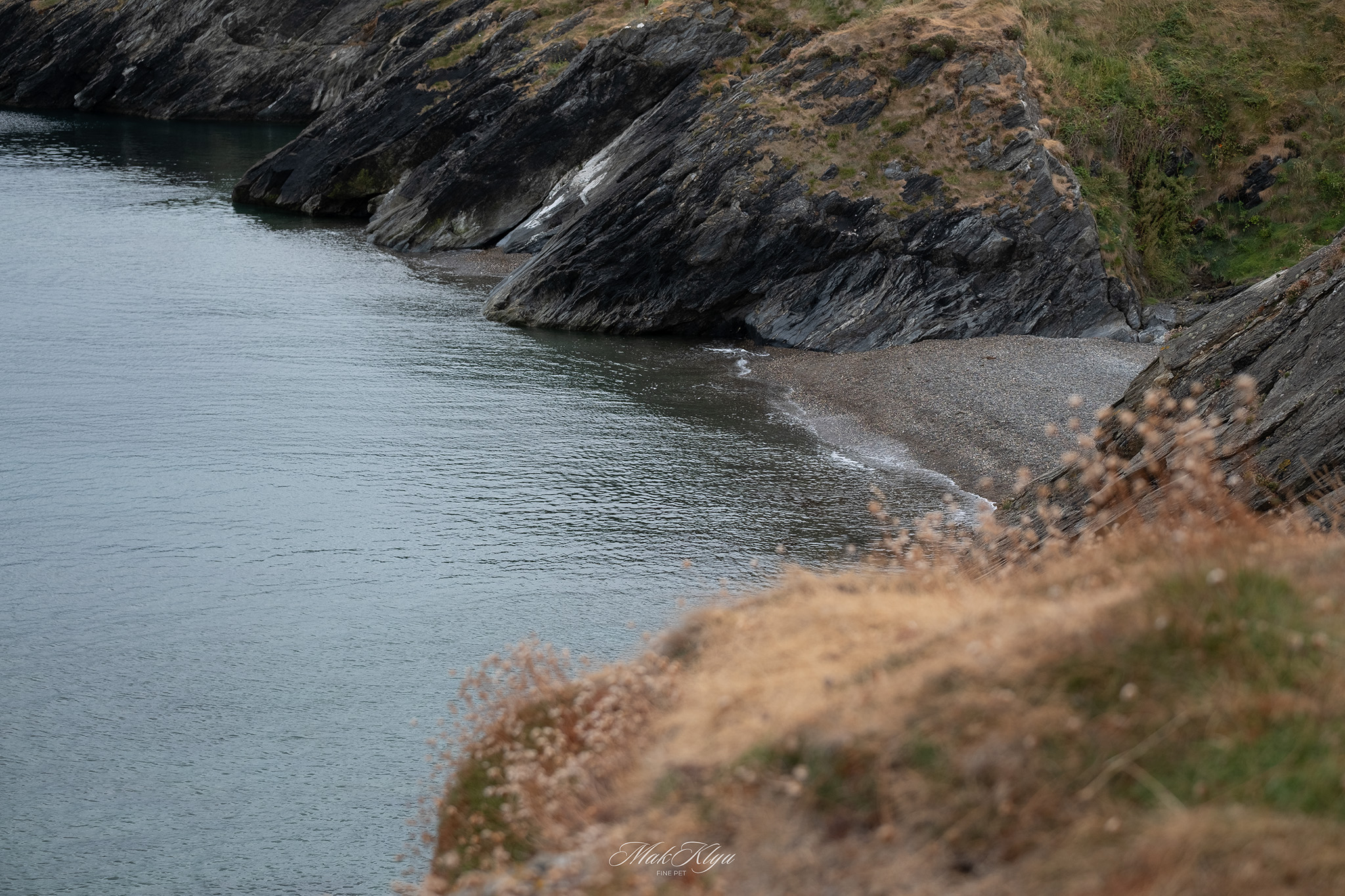 Secluded pebble beach enclosed by steep dark cliffs beside calm coastal water