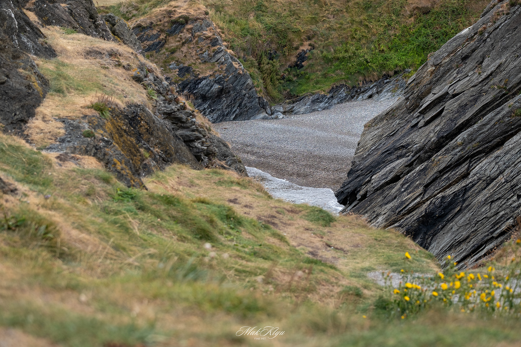 Secluded pebble beach between steep dark cliffs along a calm coastal bay